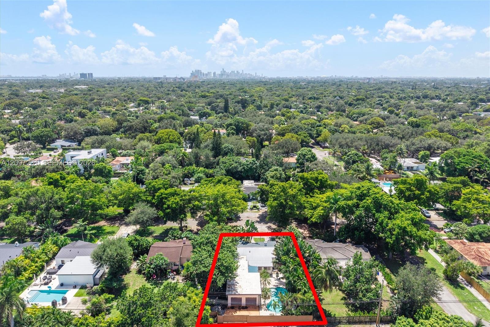 Aerial view of a home outlined in red, with a backyard pool, leafy surroundings, and a distant skyline.