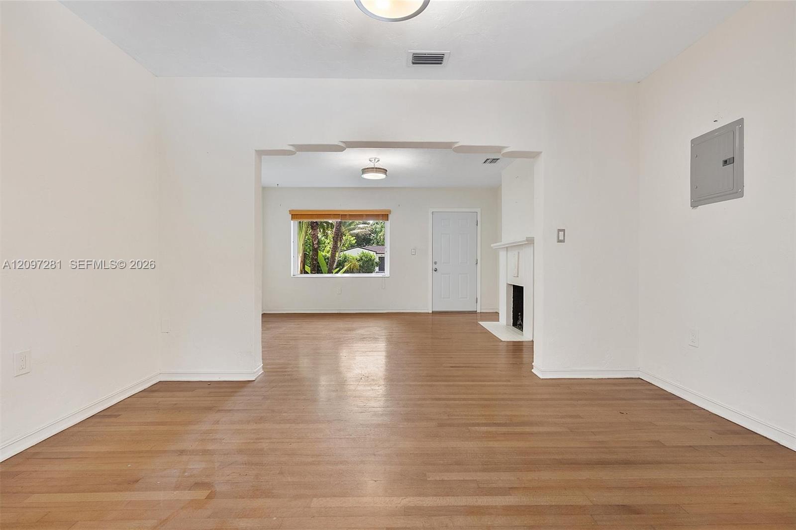 Vacant living room with hardwood floors, a fireplace, and an arched opening to the adjoining room.