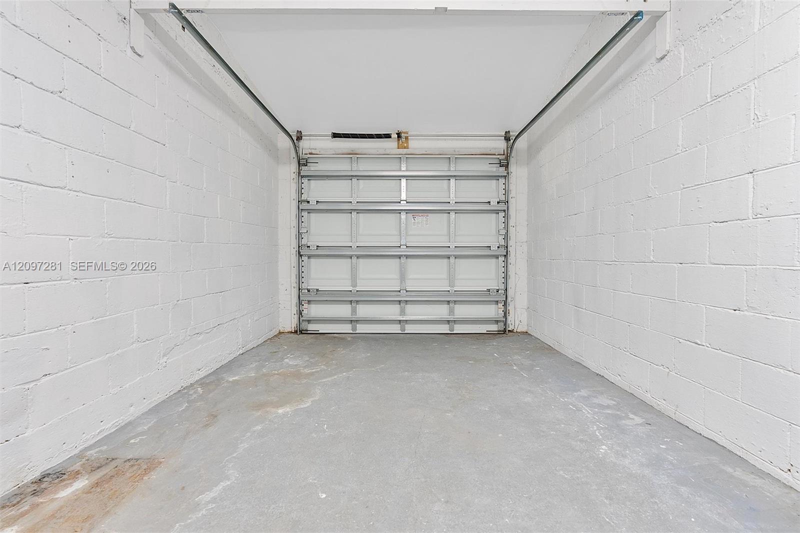 Empty garage with white cinder-block walls, a concrete floor, and a closed overhead door.