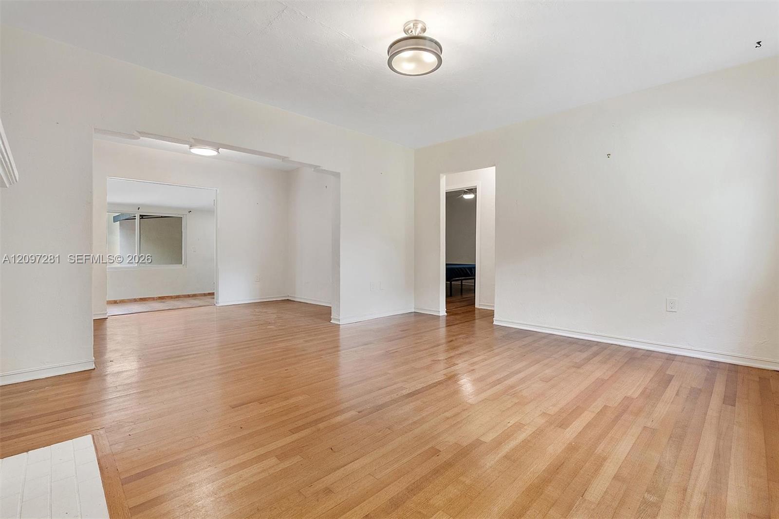 Empty room with polished hardwood floors and open doorways to adjoining rooms.