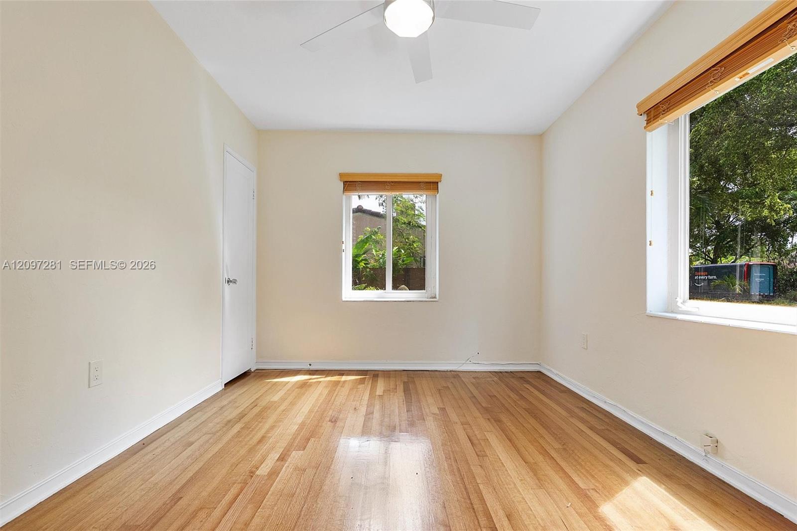 Unfurnished room with hardwood floors, a ceiling fan, and two windows with wooden blinds.