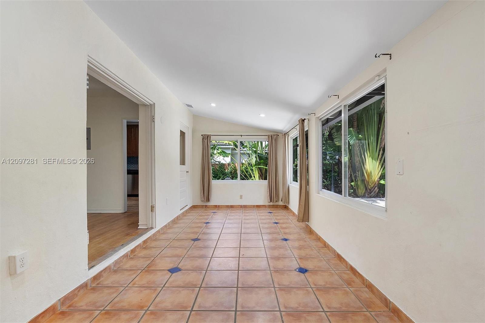 Enclosed sunroom with terracotta tile floors and large windows overlooking tropical plants.