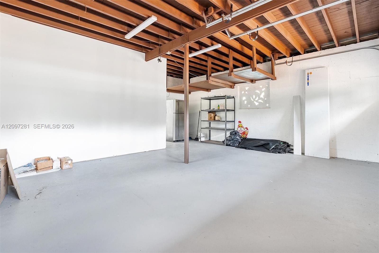 Garage with exposed wooden roof framing, concrete floor, and metal storage shelving.