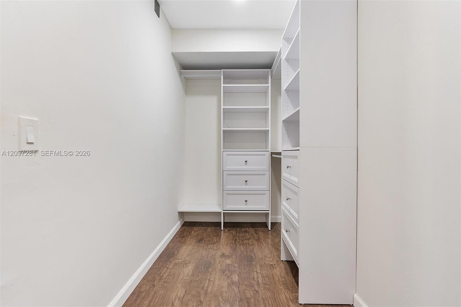 Walk-in closet with white built-in shelves and drawers and a wood-look floor.