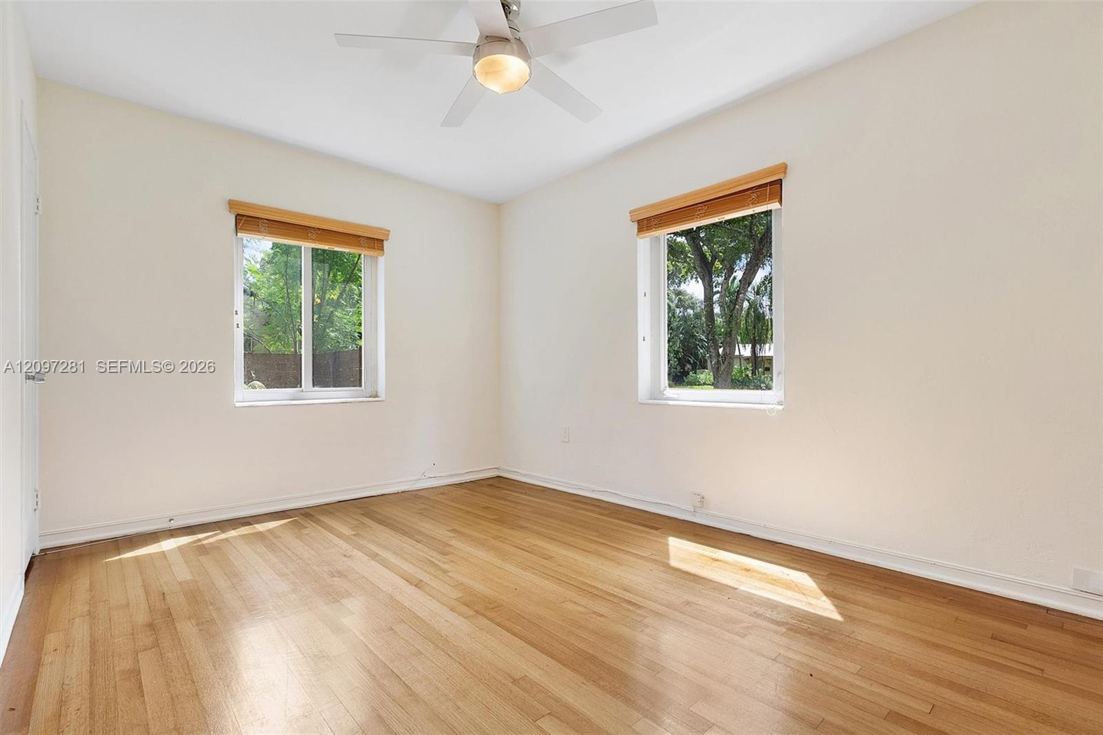 Empty room with hardwood floors, ceiling fan, and two windows with wooden blinds.