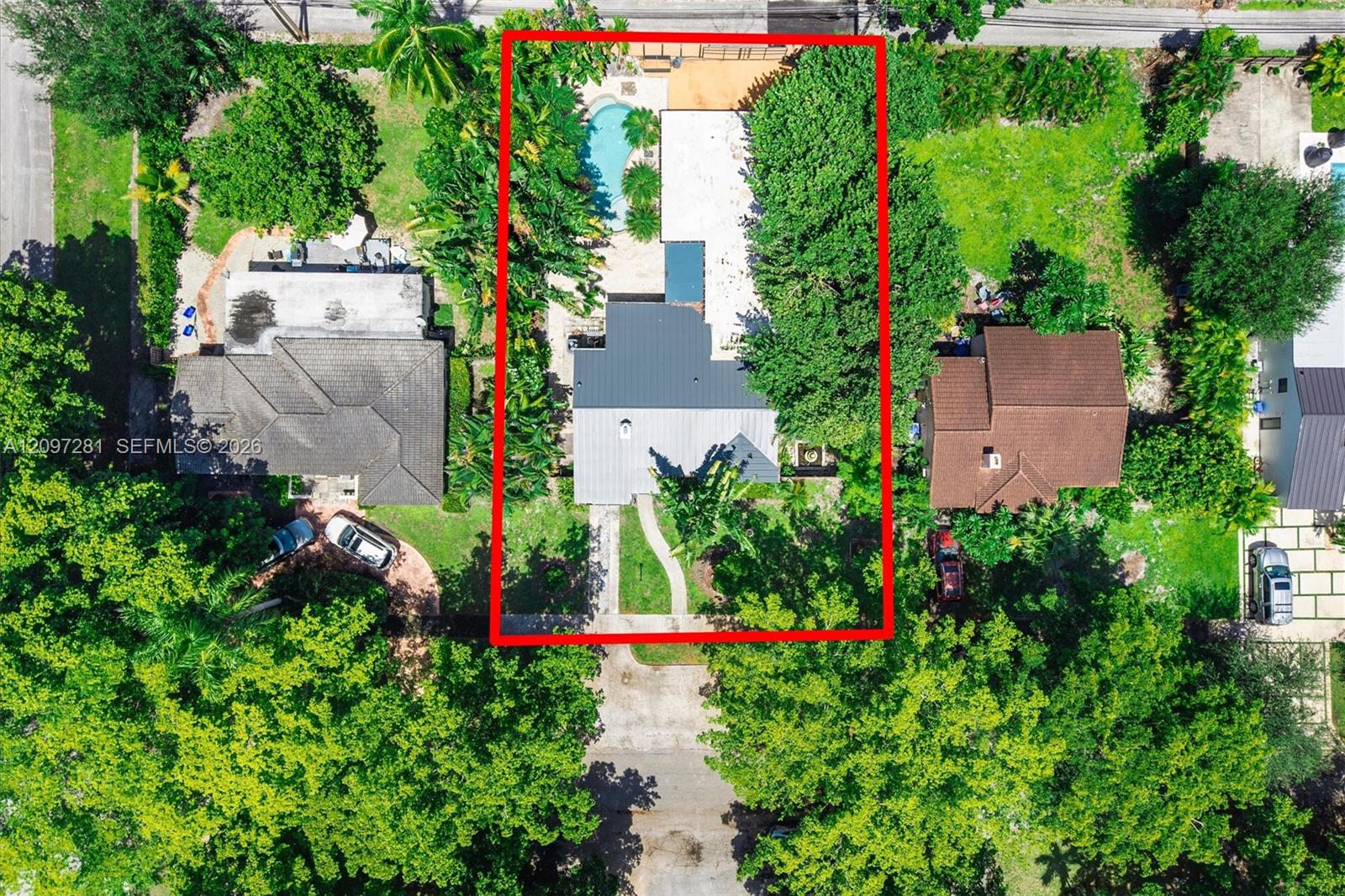 Aerial view of a home and backyard pool on a tree-filled lot outlined in red.