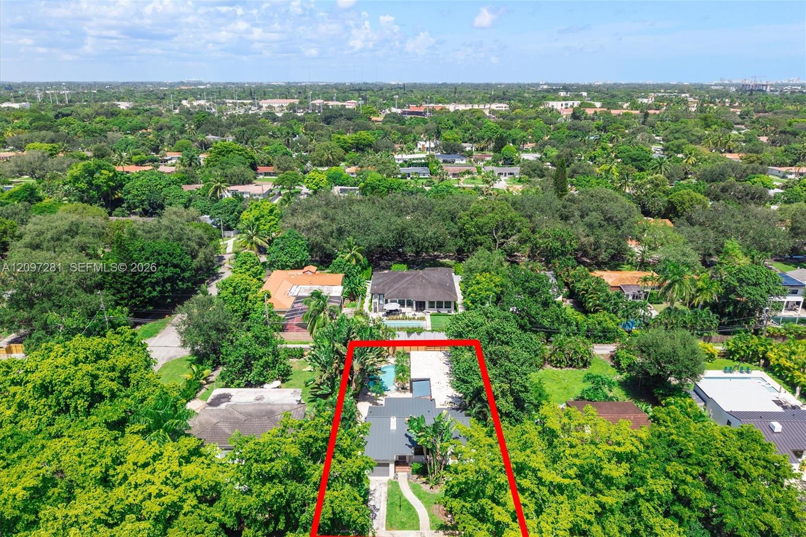 Aerial view of a house and swimming pool on a tree-lined lot outlined in red.