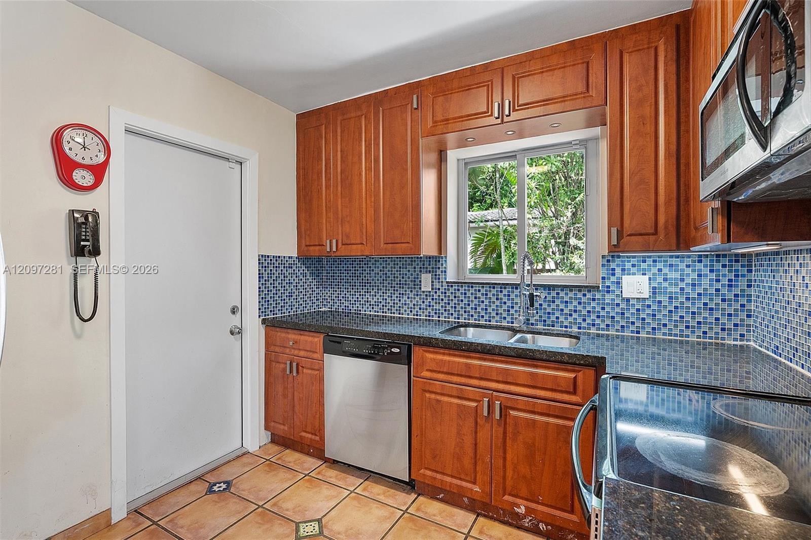 Kitchen with reddish-brown cabinets, blue mosaic backsplash, and a double sink beneath a window.