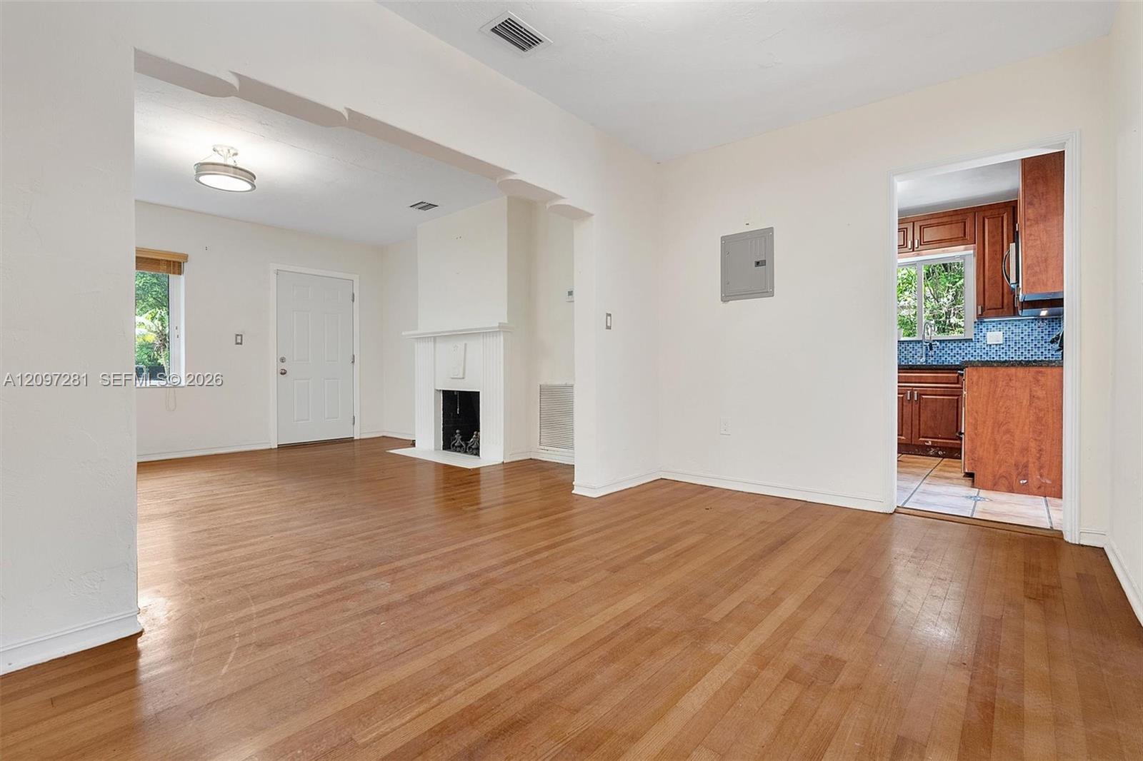 Living room with hardwood floors and a white fireplace, opening to a wood-cabinet kitchen.