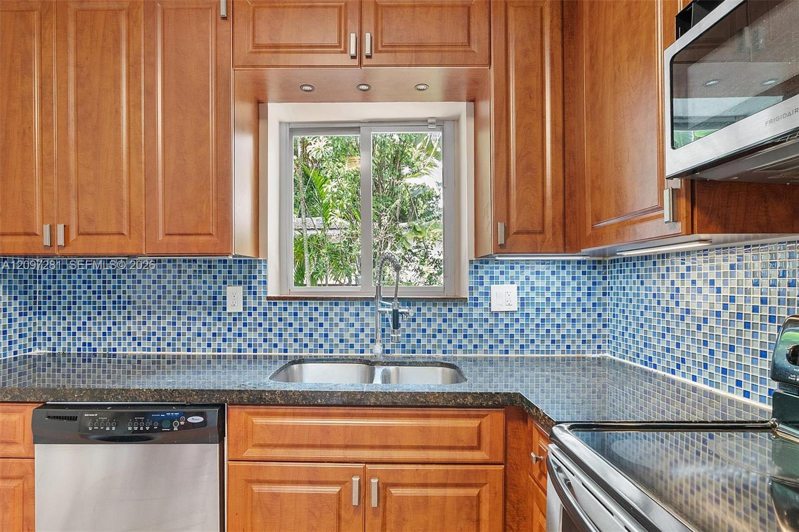 Kitchen with wood cabinets, blue mosaic backsplash, and double sink beneath a window.