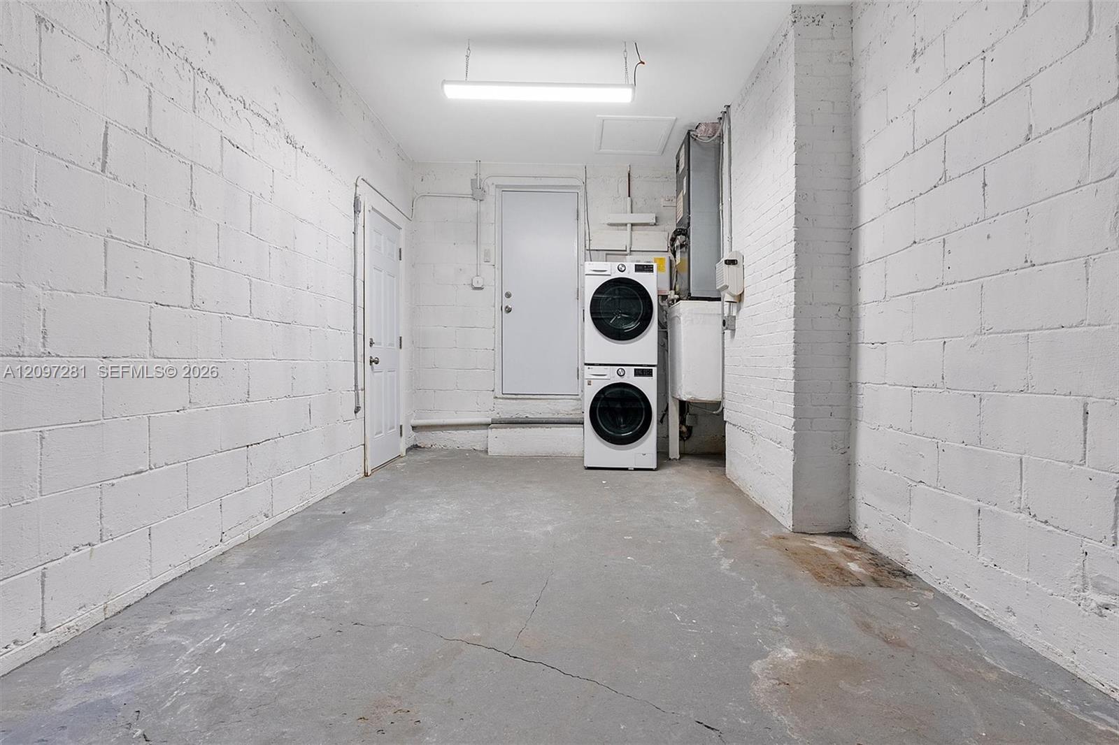 Laundry room with a stacked washer and dryer, white block walls, and concrete floor.
