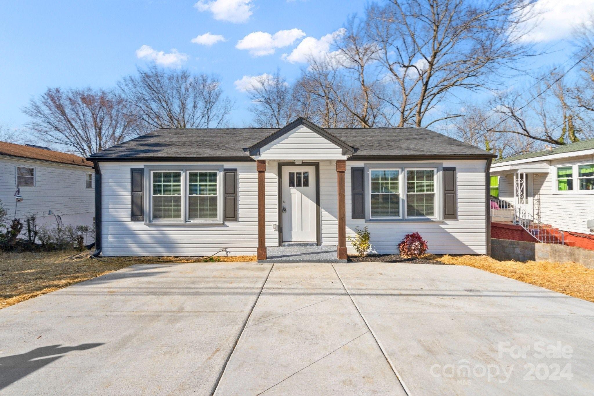 Single-story light-sided house with a covered entry and broad concrete driveway.