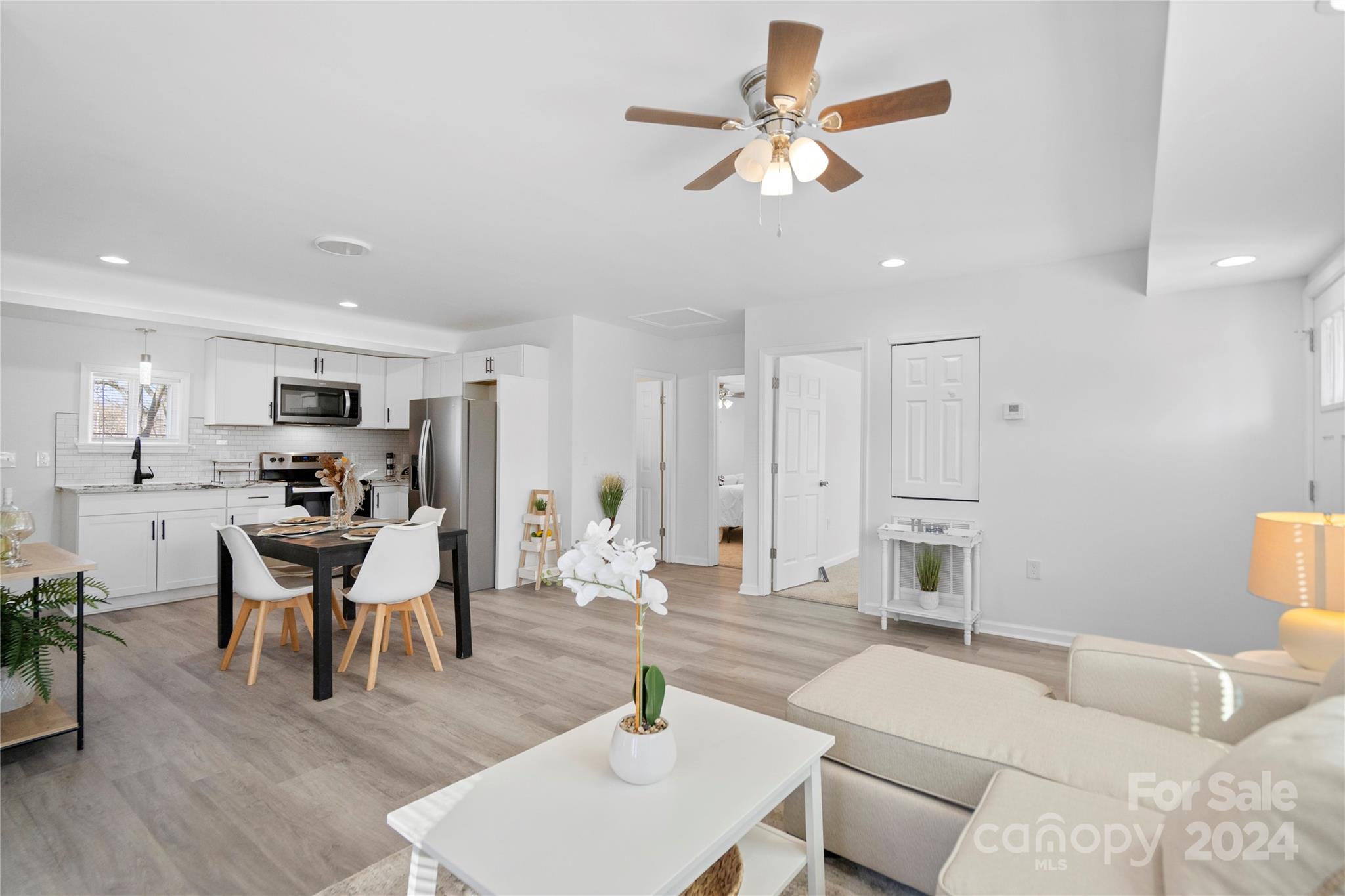 Open-plan kitchen and living room with white cabinetry, stainless appliances, and a dining table.