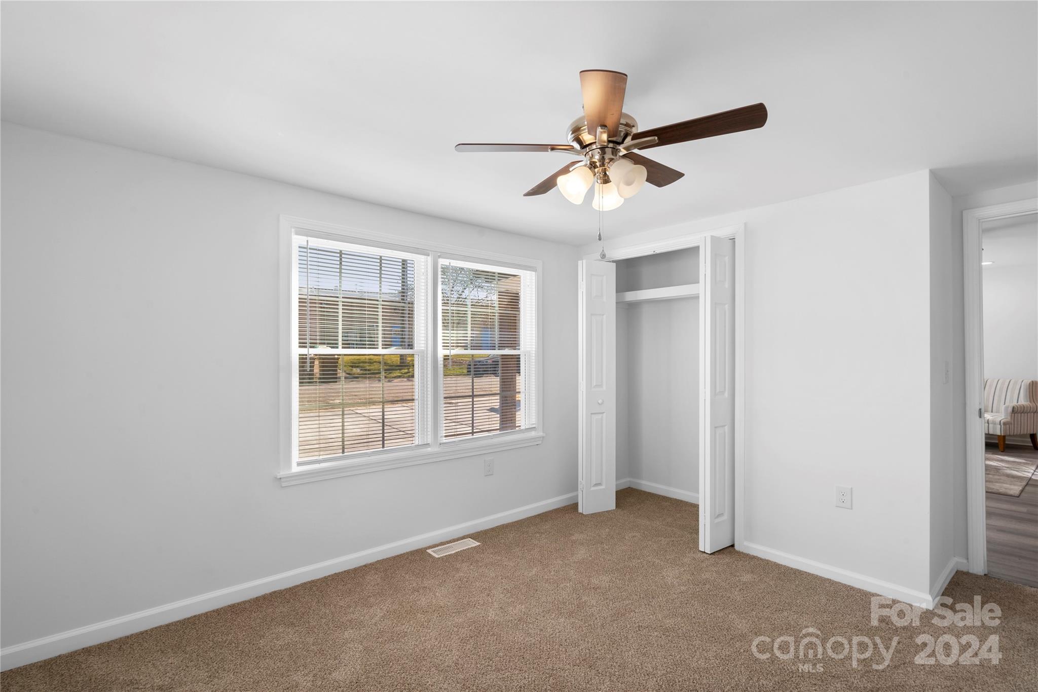 Unfurnished bedroom with beige carpet, a ceiling fan, two windows, and an open closet.
