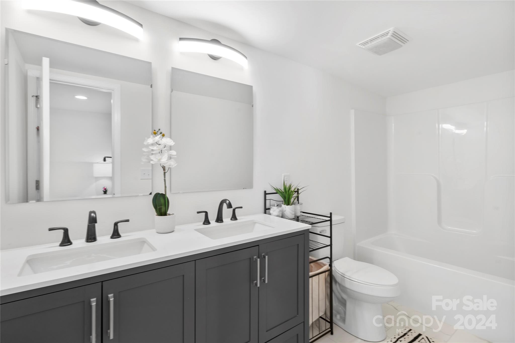 Bathroom with a double-sink dark gray vanity, large mirrors, and a white tub-shower enclosure.