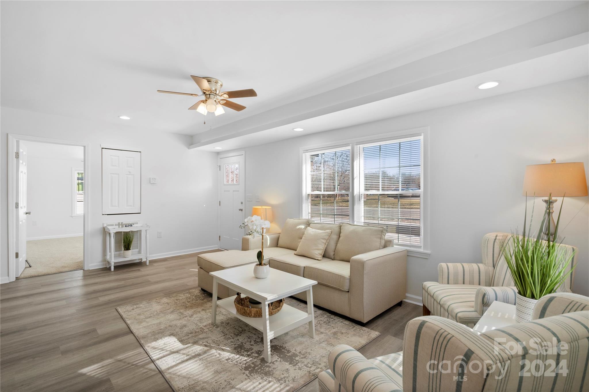Staged living room with a beige sectional, striped armchairs, and large windows with blinds.