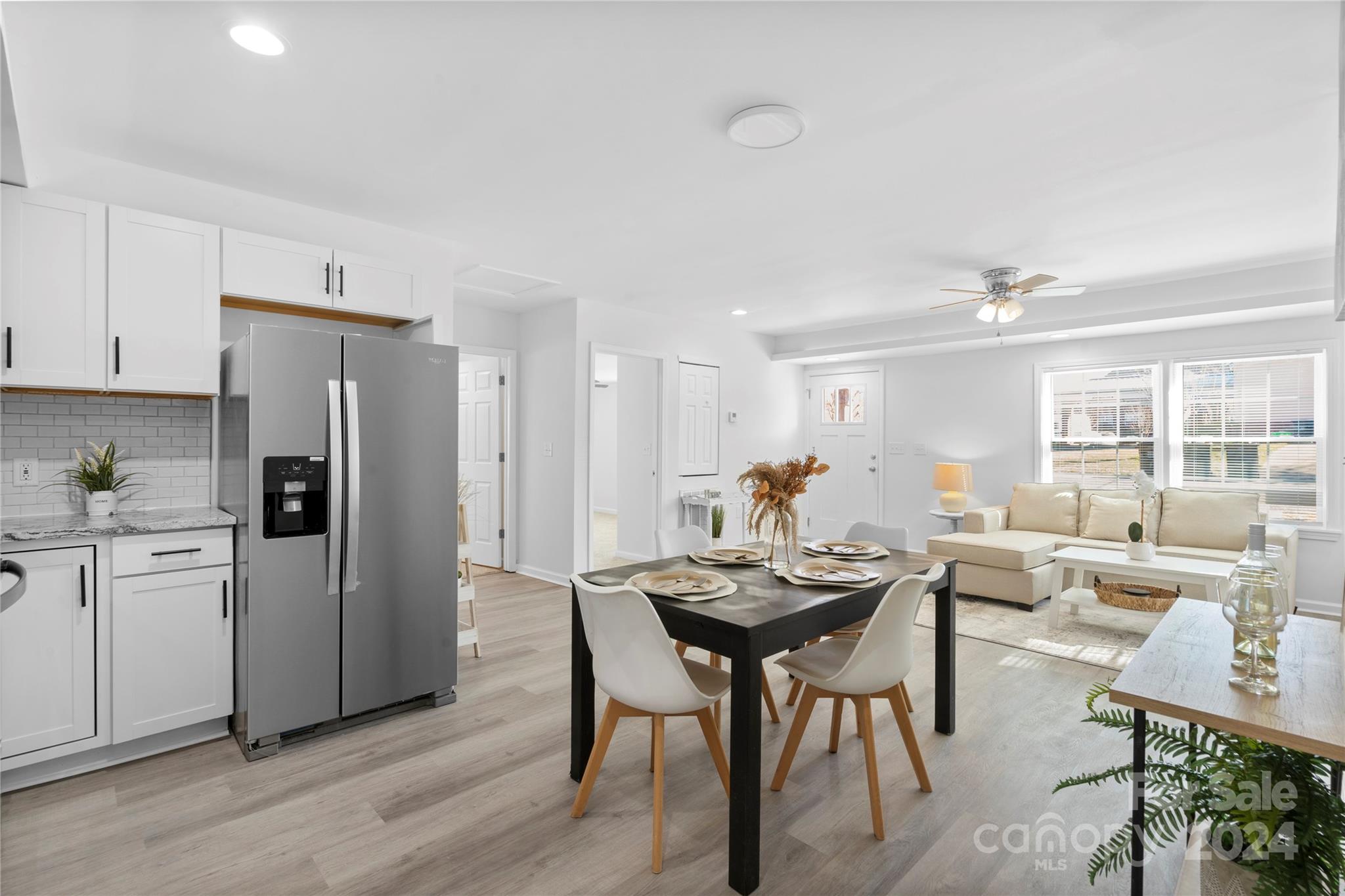 Open-plan kitchen and living room with a set dining table, white cabinetry, and a cream sectional by large windows.