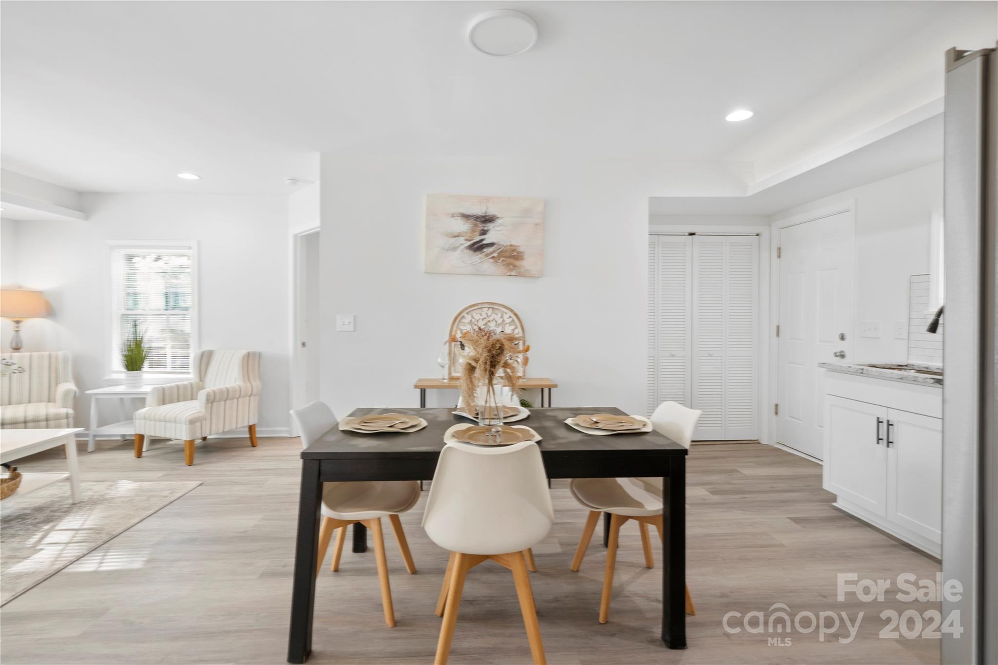 Staged dining area with a dark table set for four, open to a bright sitting area and white kitchen.