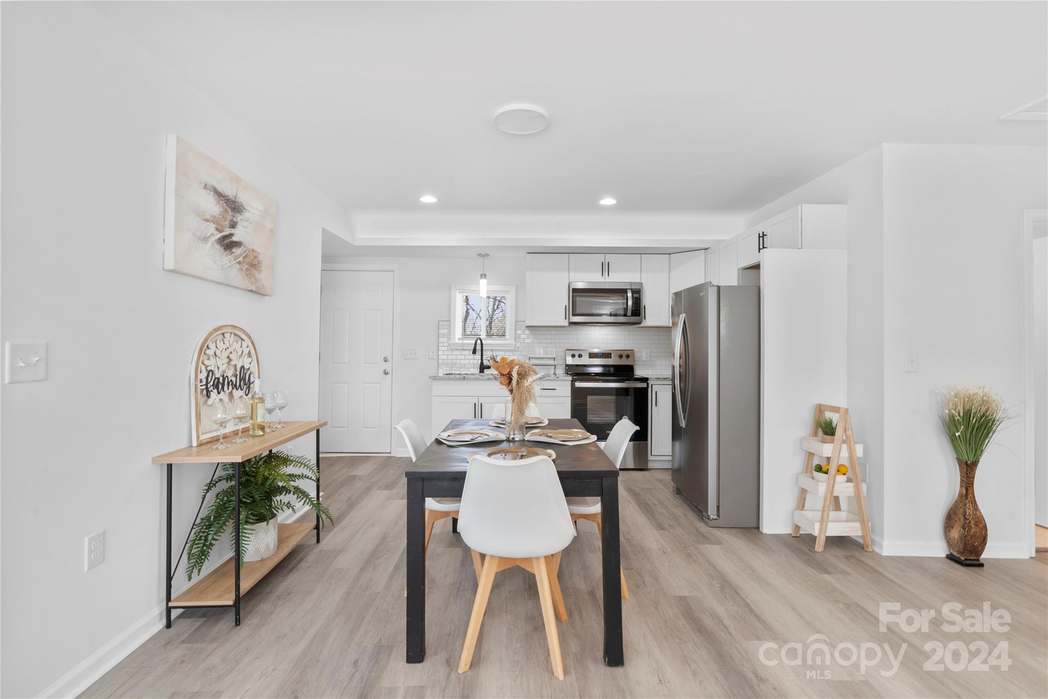 Open-plan kitchen and dining area with white cabinets, stainless steel appliances, and a set dining table.