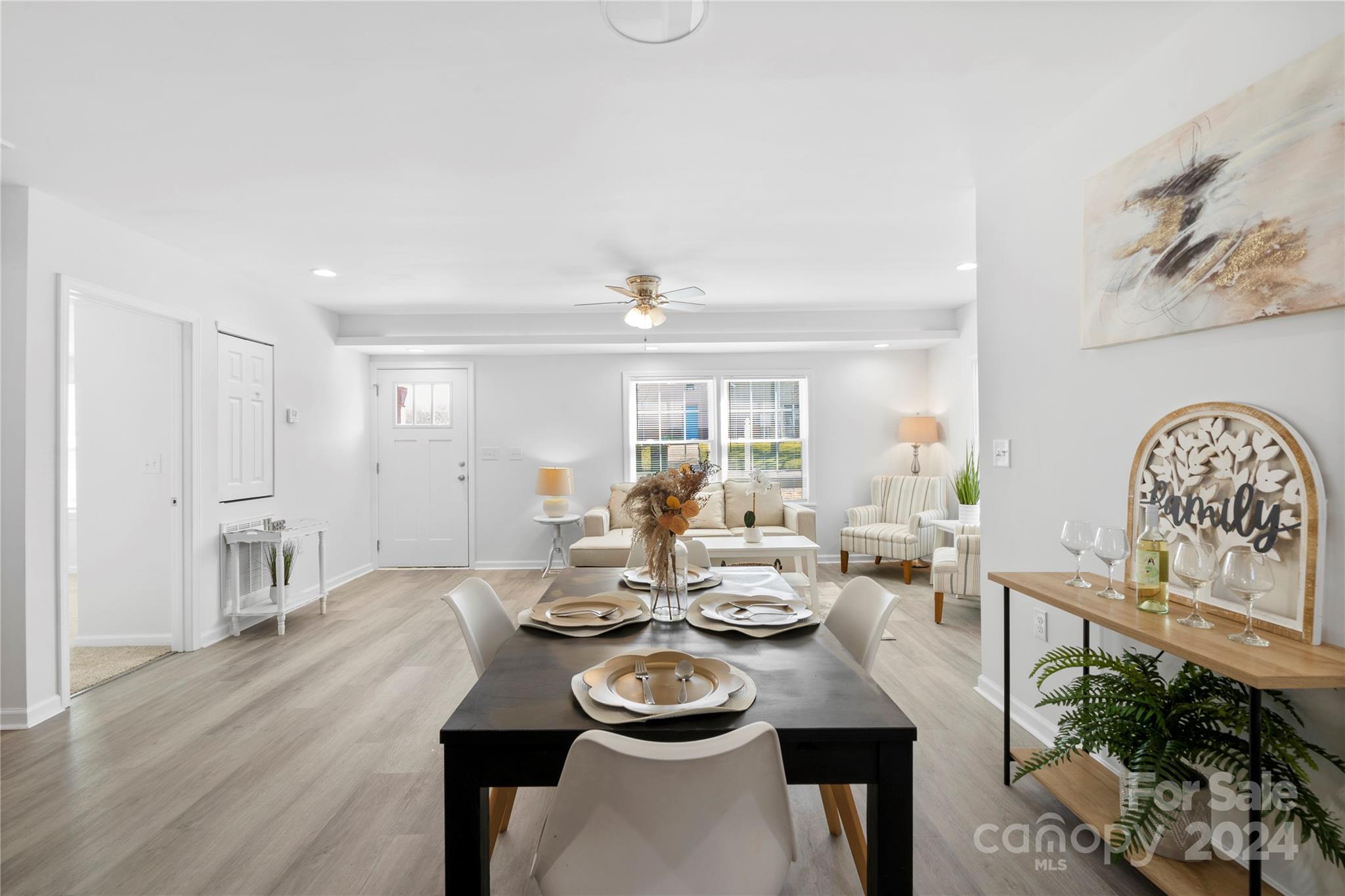 Staged dining and living area with a set black table, white sofa, and striped armchairs.