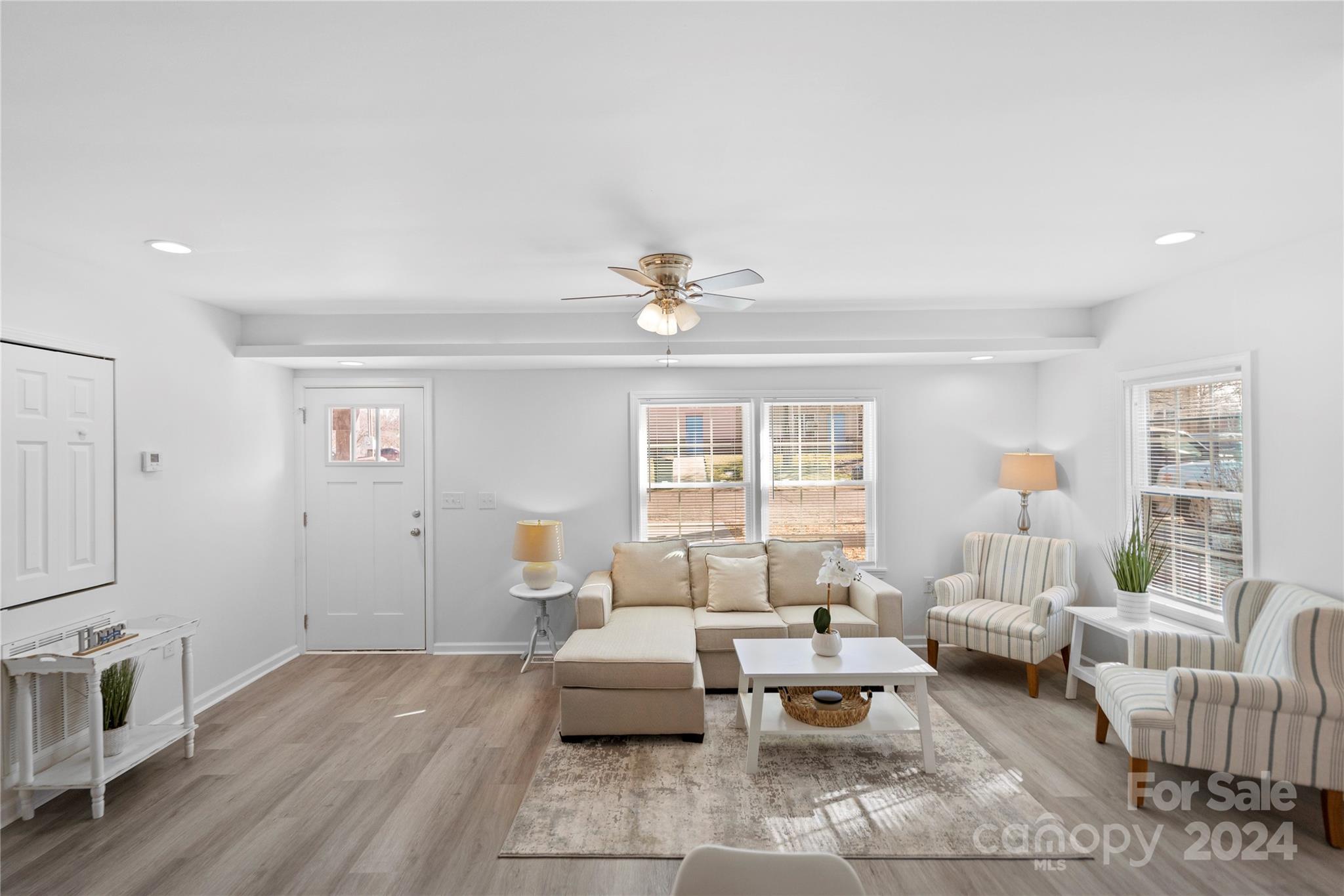 Furnished living room with a beige sectional, striped armchairs, and large windows with blinds.