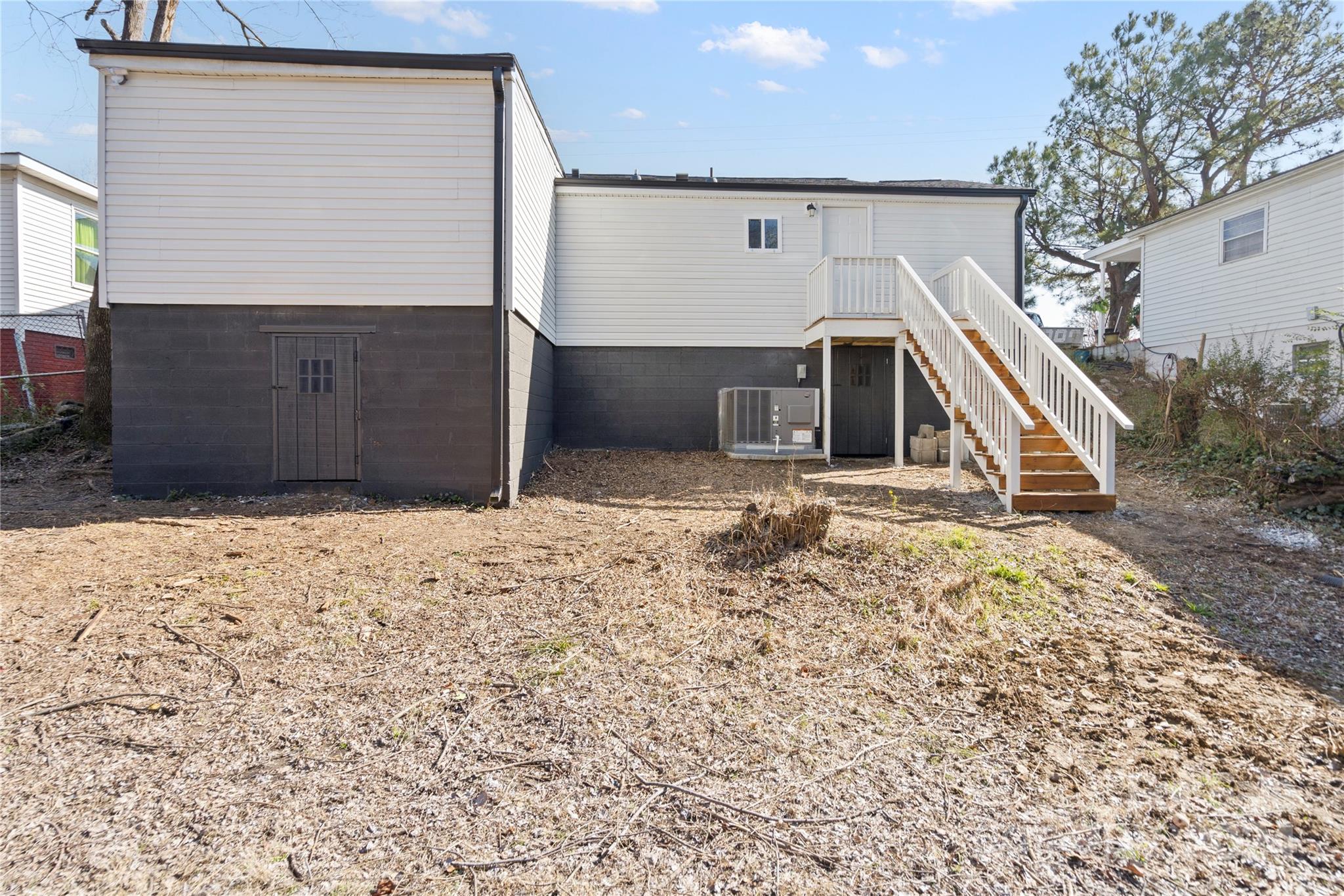 Rear of a raised home with white siding, an exterior staircase, and a broad dormant yard.