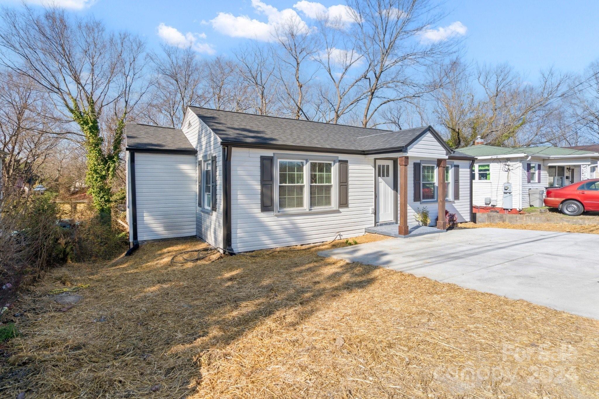 Single-story gray-sided house with dark shutters, brick porch columns, and a concrete driveway.