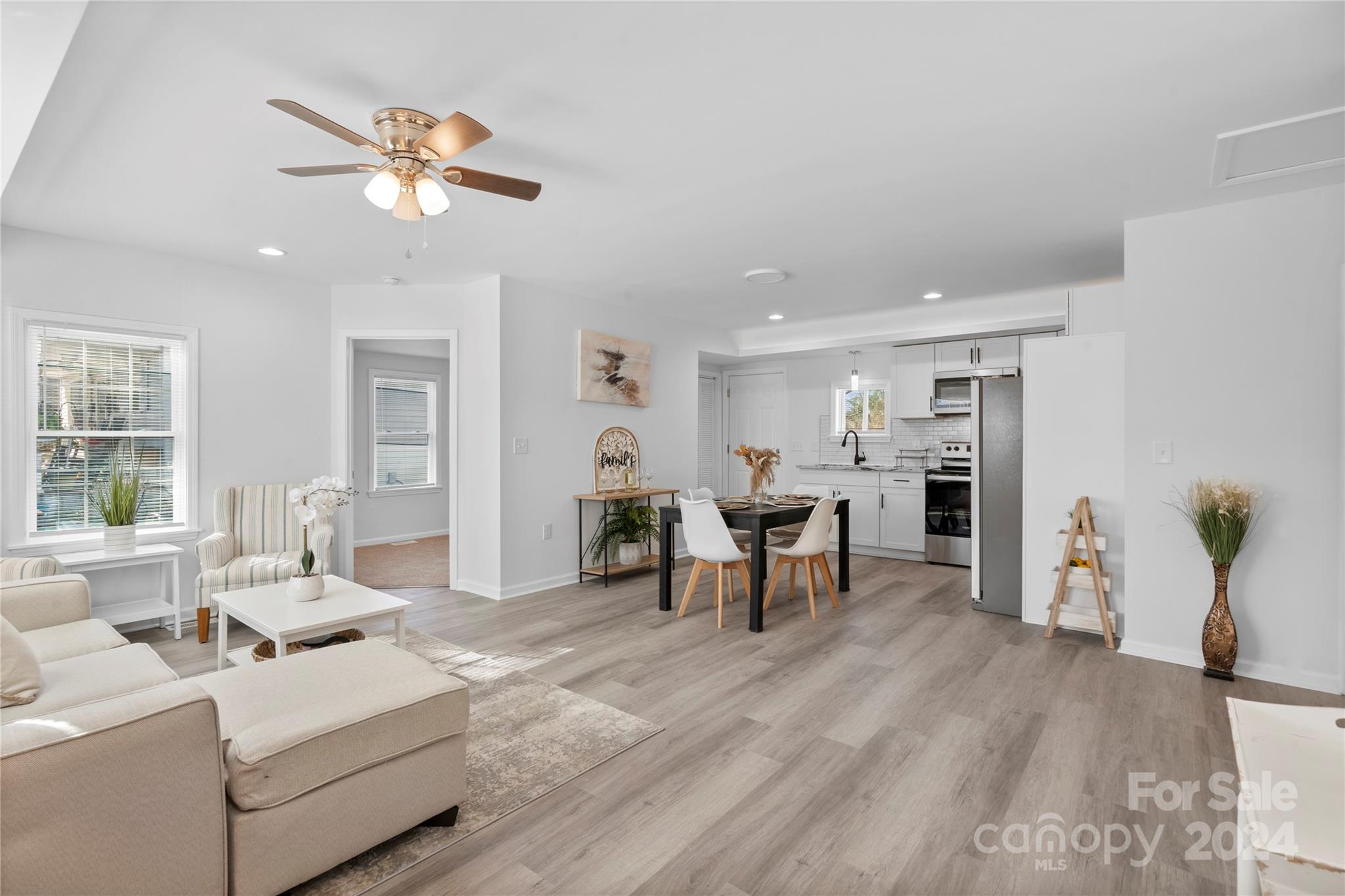 Open-plan living and dining area with a white kitchen, stainless steel appliances, and light wood-look floors.