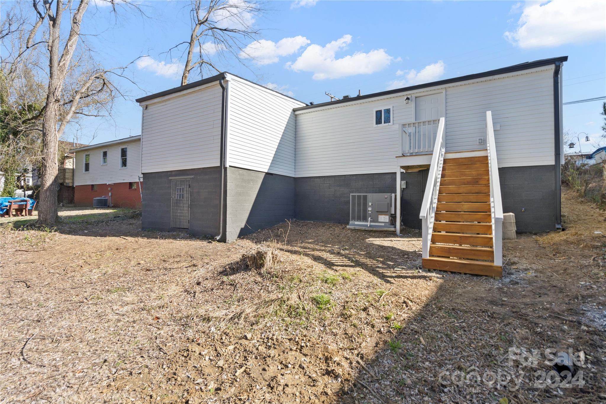 Rear of a white-sided house with a dark foundation and raised wooden stairs leading to the upper level.