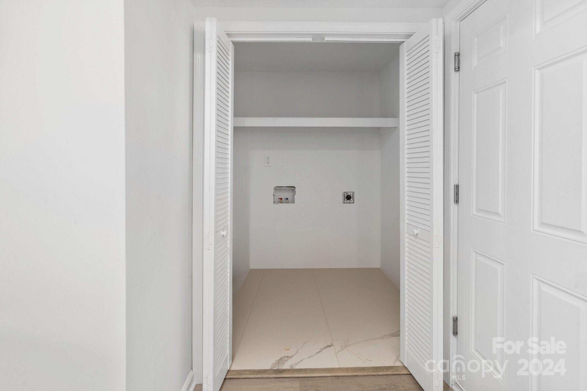Empty laundry closet with open louvered doors, a shelf, and washer and dryer hookups.