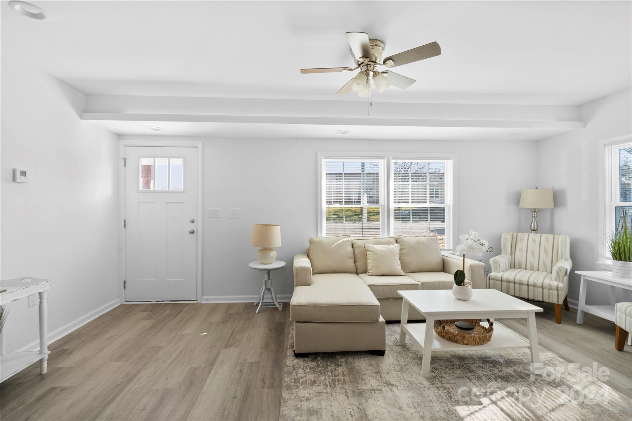 Staged living room with a beige sectional, striped armchair, white coffee table, and bright front windows.