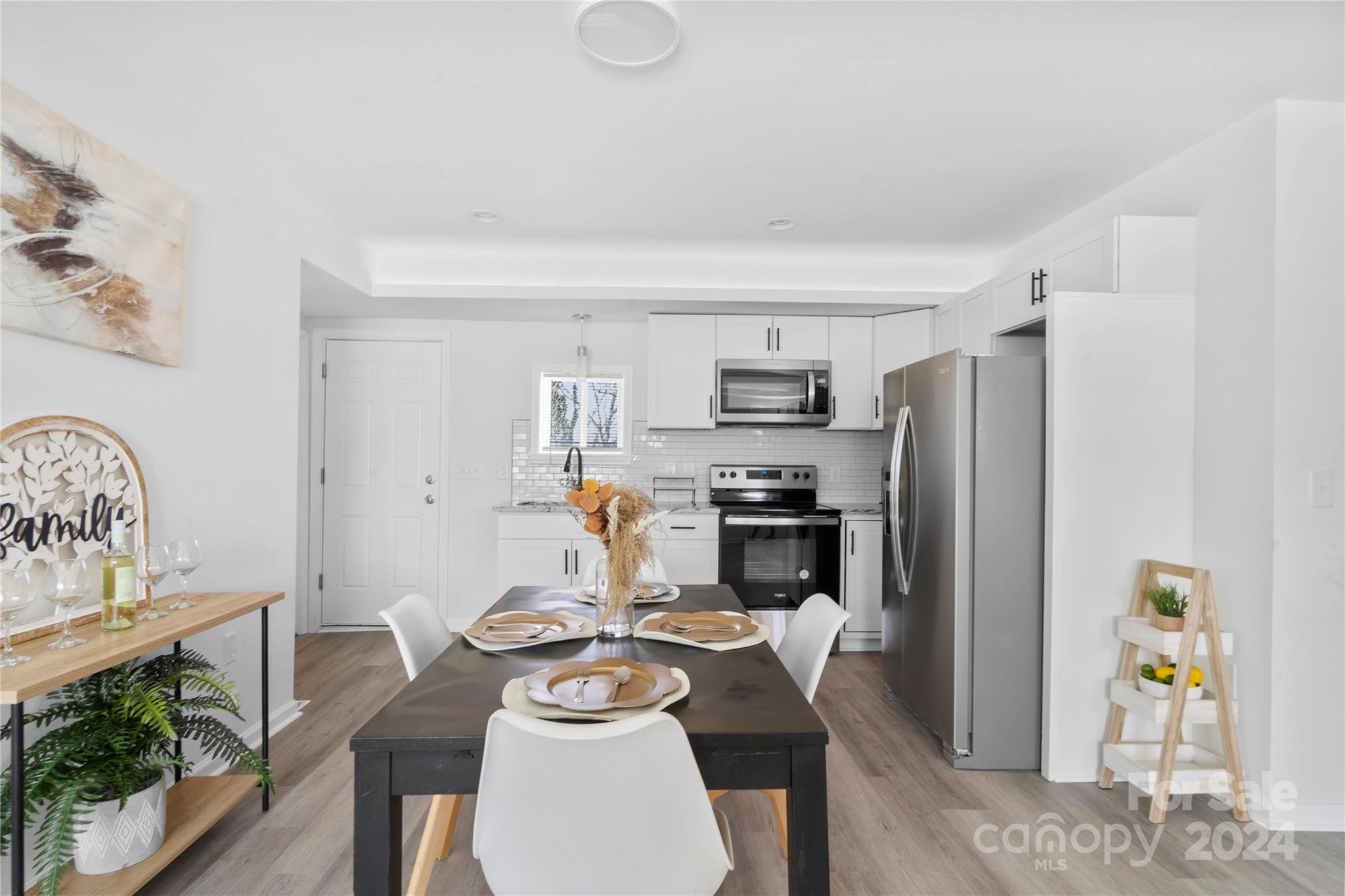 Staged kitchen and dining area with white cabinets, stainless steel appliances, and a table set for dining.