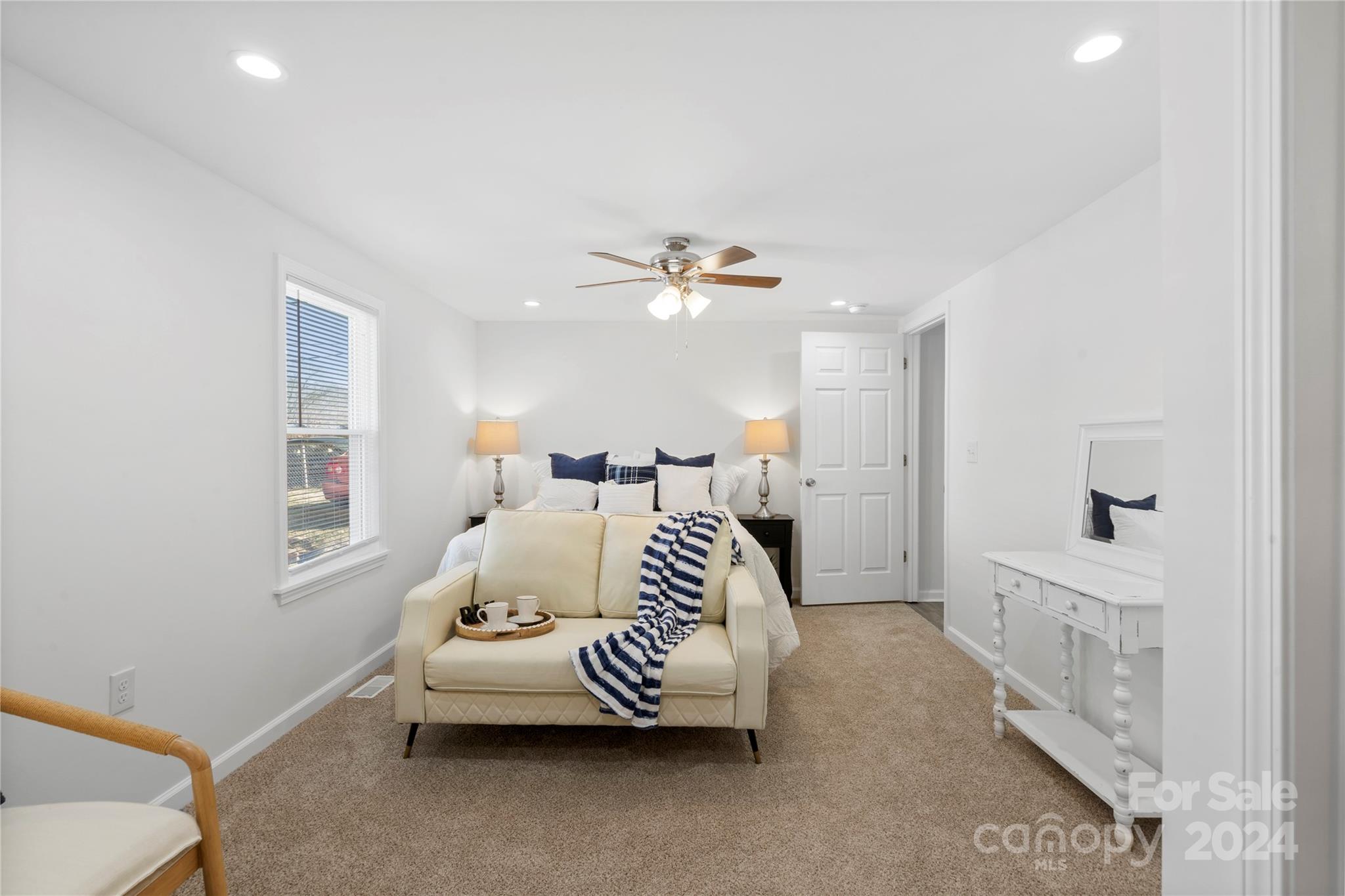 Staged bedroom with a cream loveseat and striped throw in front of a bed.