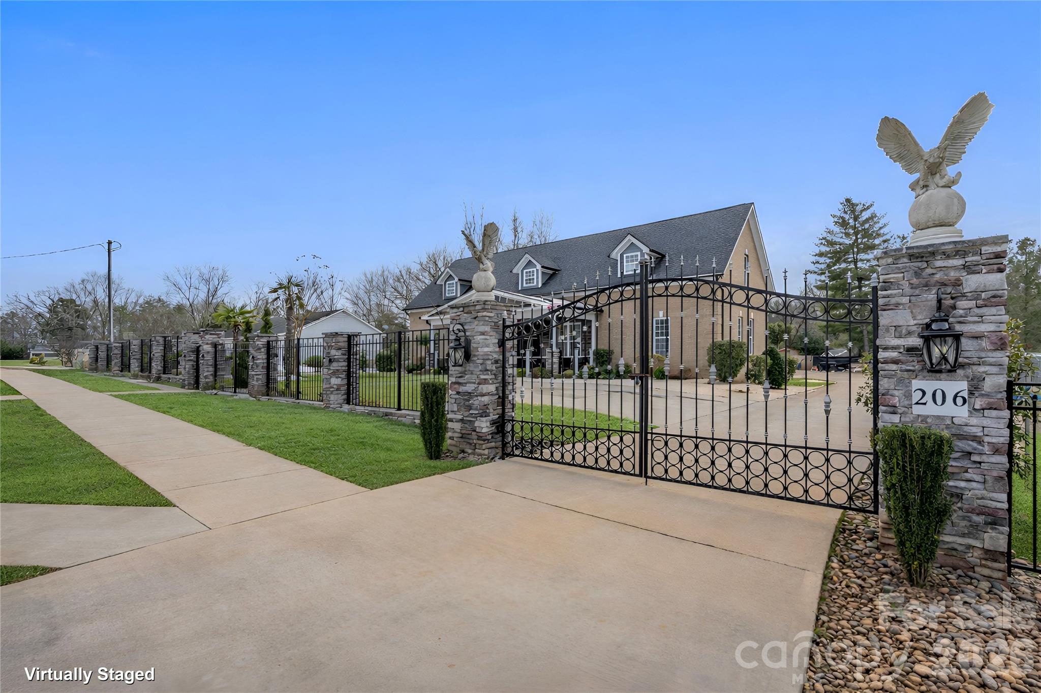 Brick home behind an ornate iron gate, with stone pillars topped by eagle sculptures and a broad driveway.