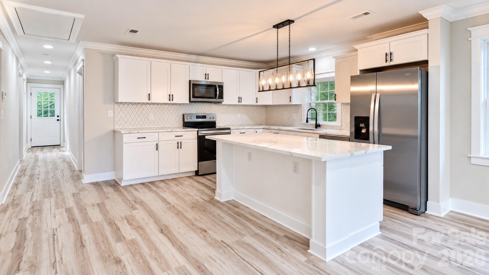 Renovated kitchen with a large island, white cabinets, stainless steel appliances, and light wood-look floors.