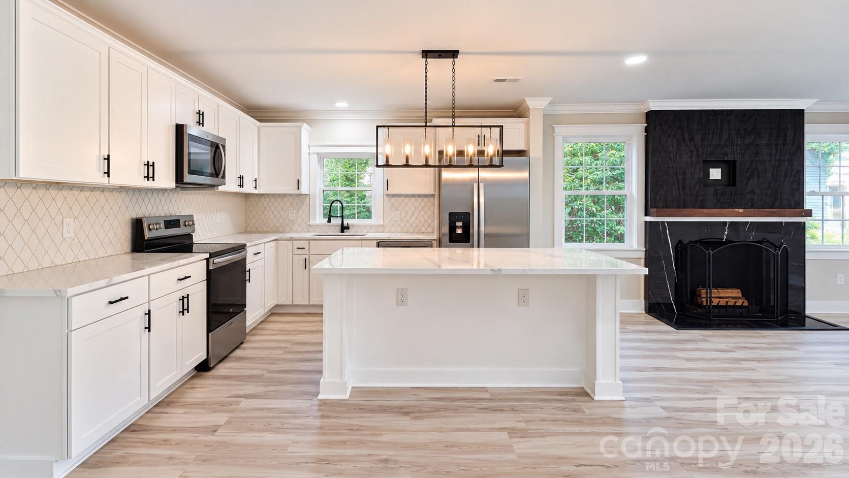 Renovated kitchen with white cabinets, a large island, stainless steel appliances, and a black fireplace.