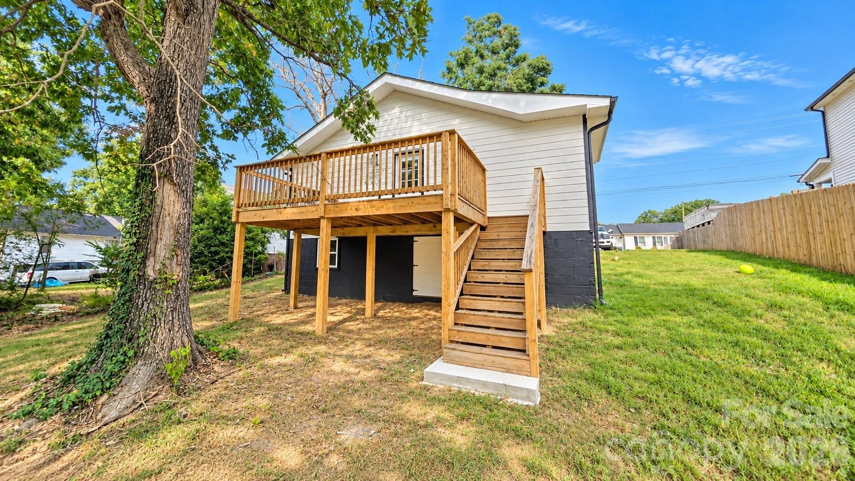 White house with a raised wooden deck and stairs opening onto a grassy, fenced backyard.