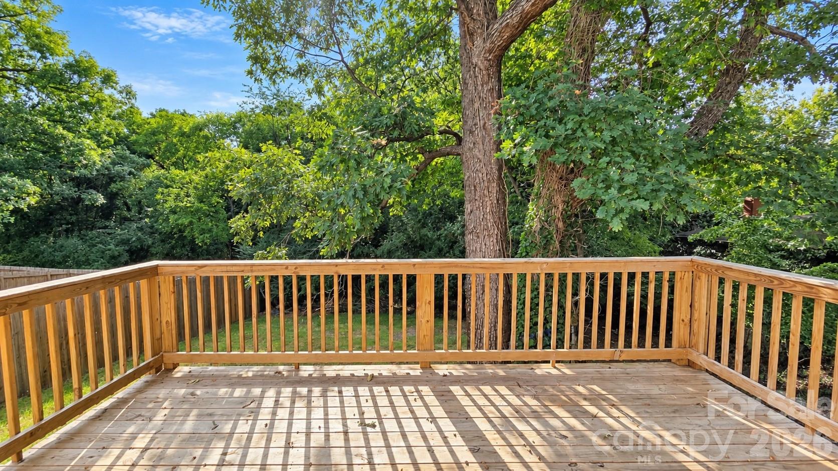 Wooden deck with railings overlooking a shaded, tree-filled backyard.