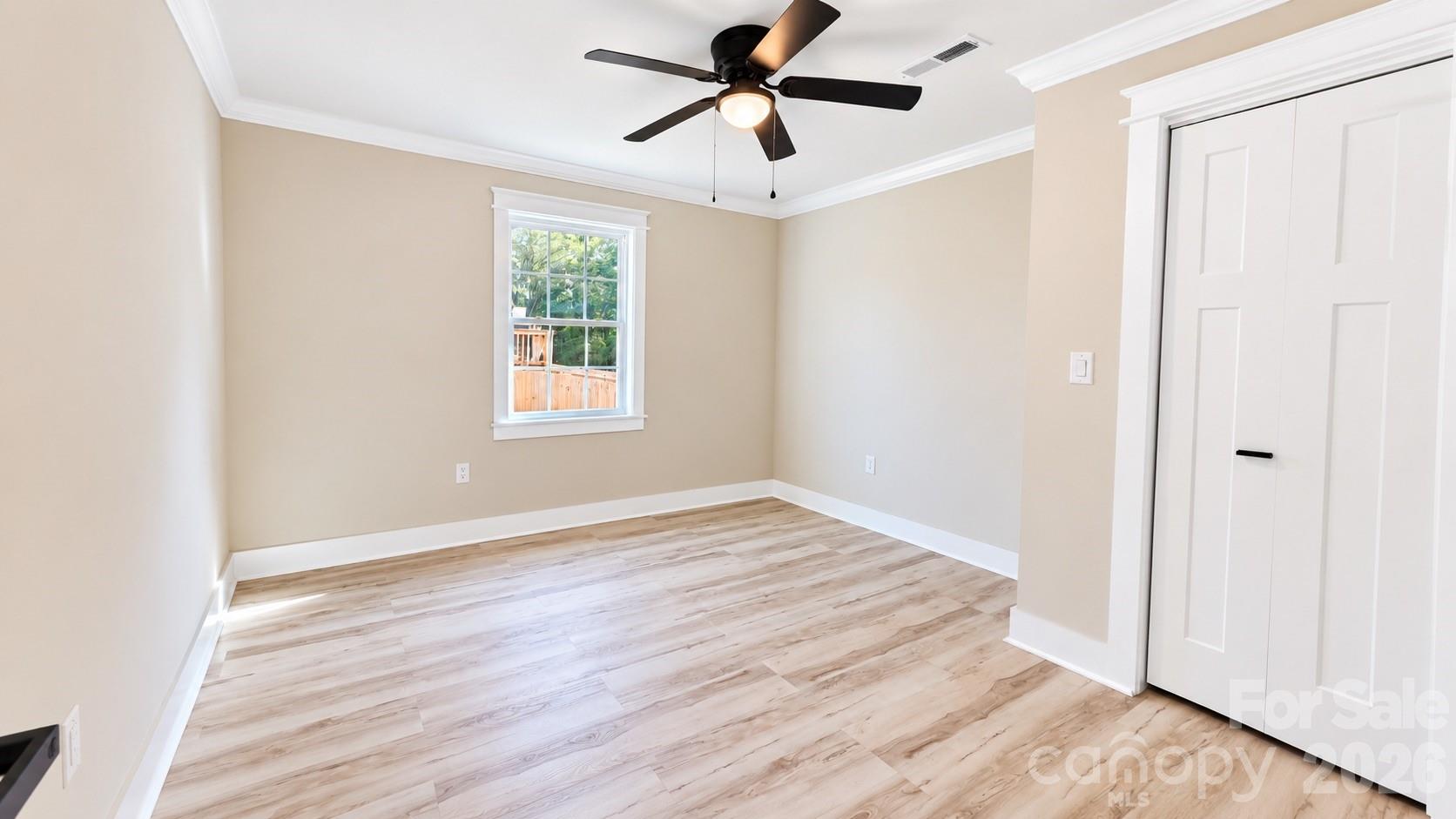 Empty bedroom with light wood flooring, ceiling fan, and white closet doors.