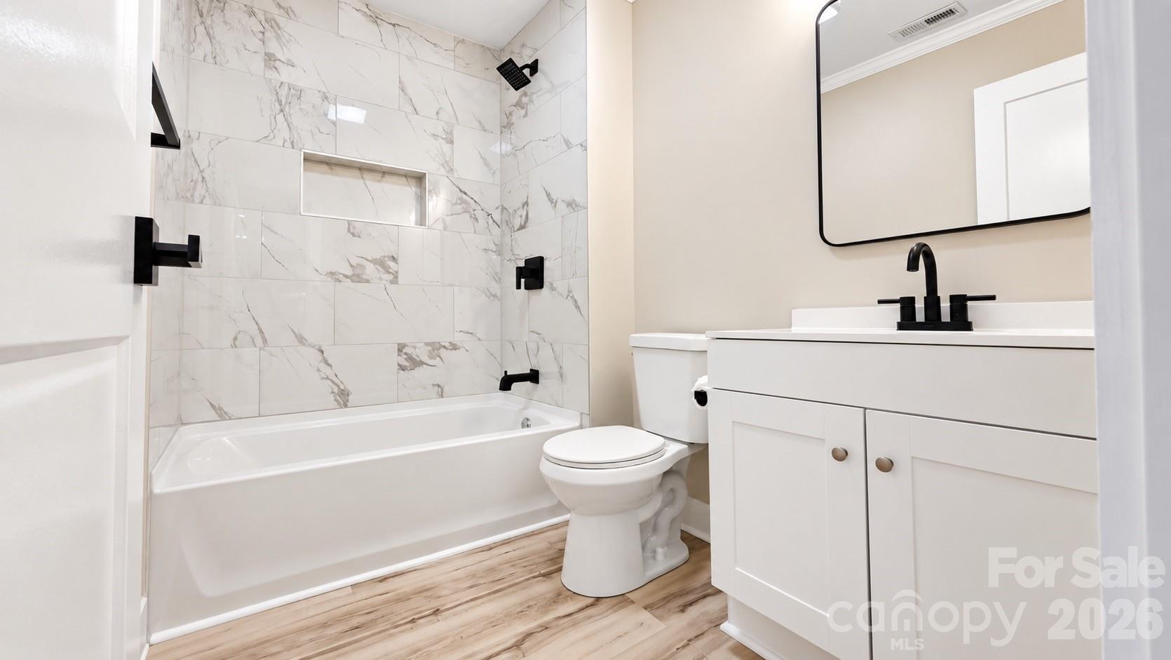 Renovated bathroom with marble-look shower tile, matte black fixtures, and a white vanity.