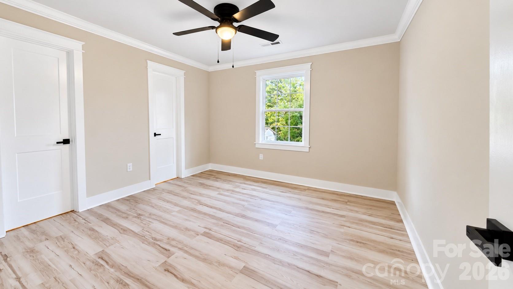 Vacant bedroom with light wood-look floors, a black ceiling fan, and a white-trimmed window.