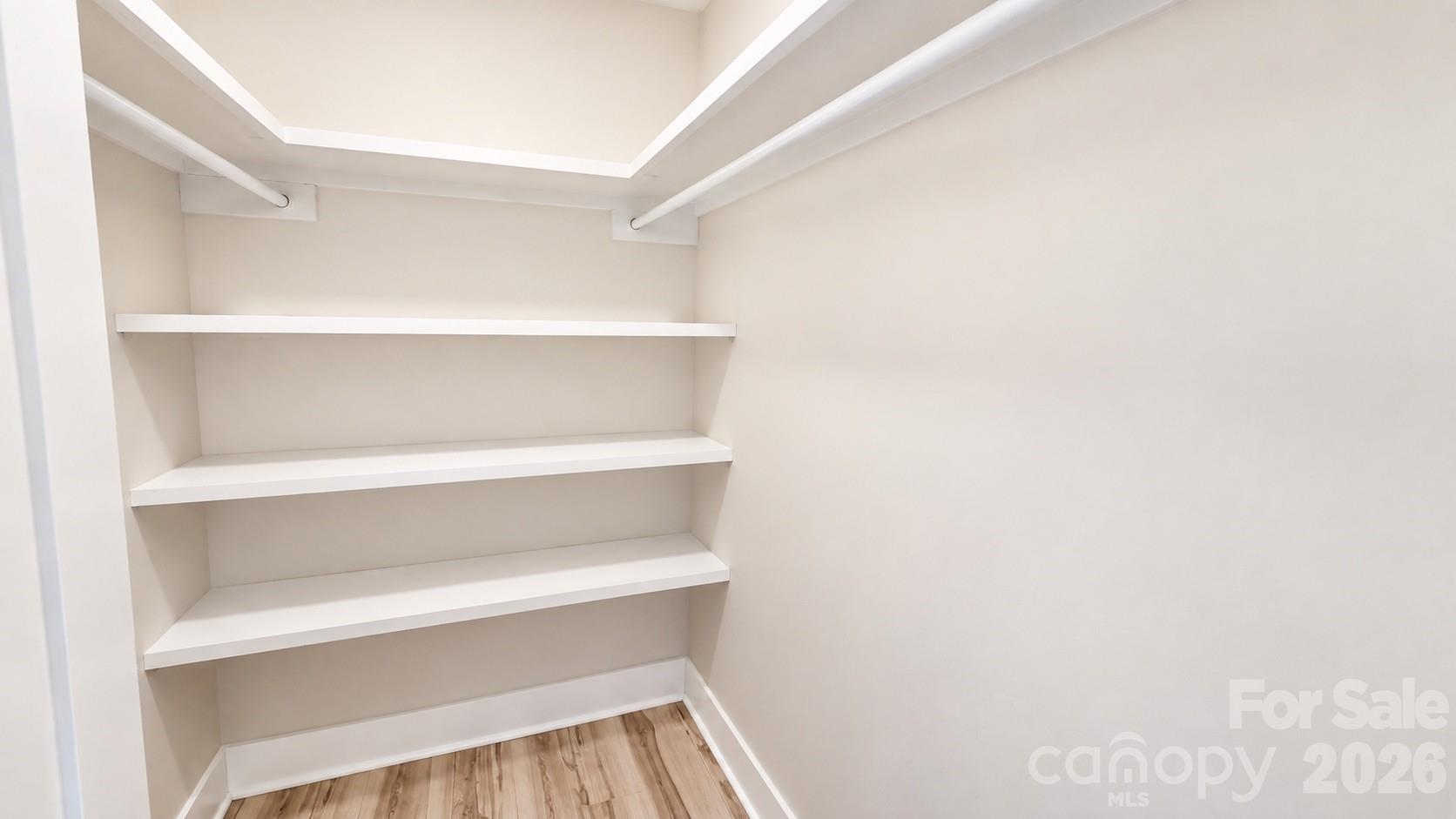 Empty walk-in closet with three built-in shelves, hanging rods, and wood-look flooring.