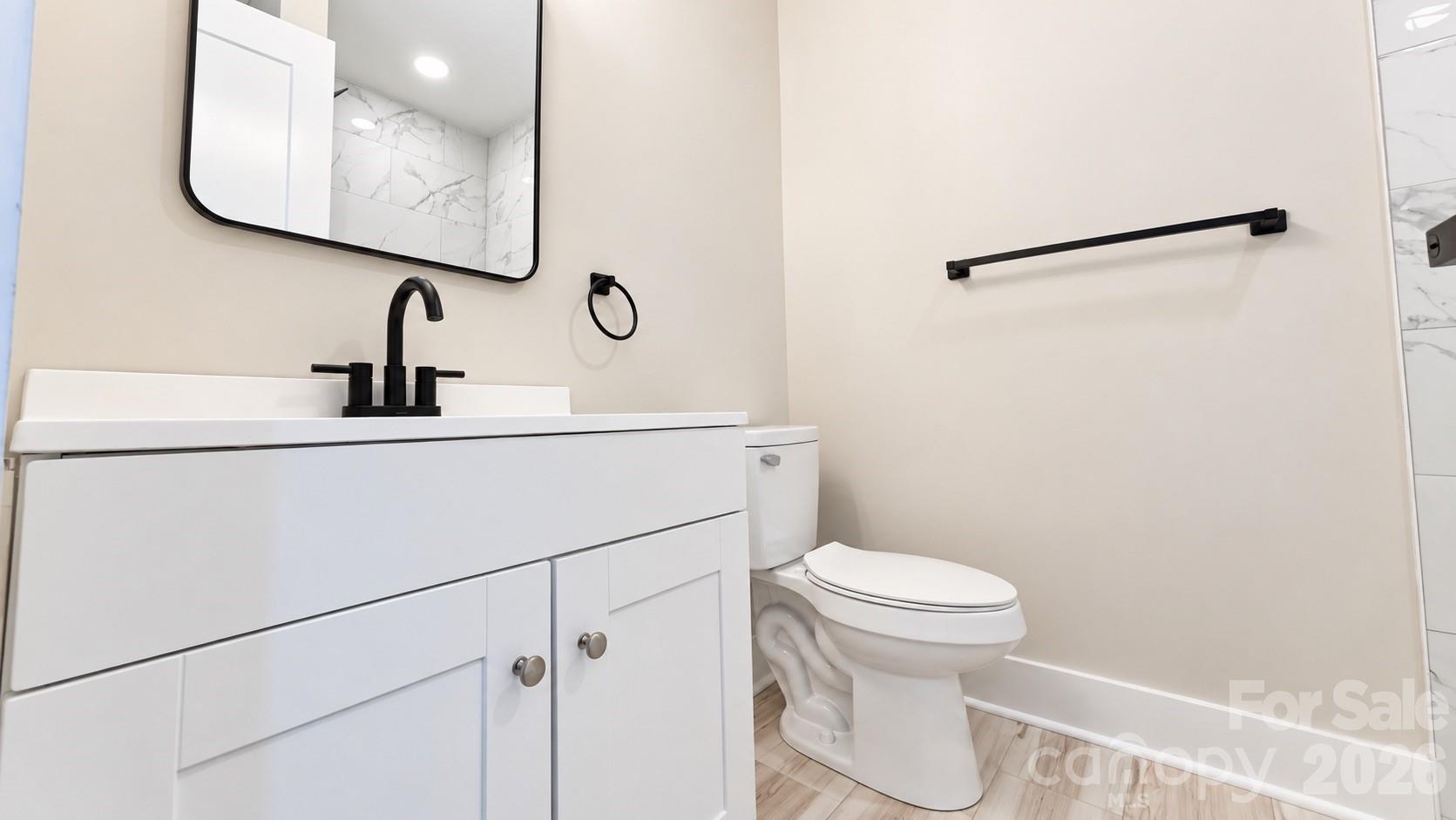 Bathroom with a white vanity, black fixtures, and a toilet beside a light wood-look floor.