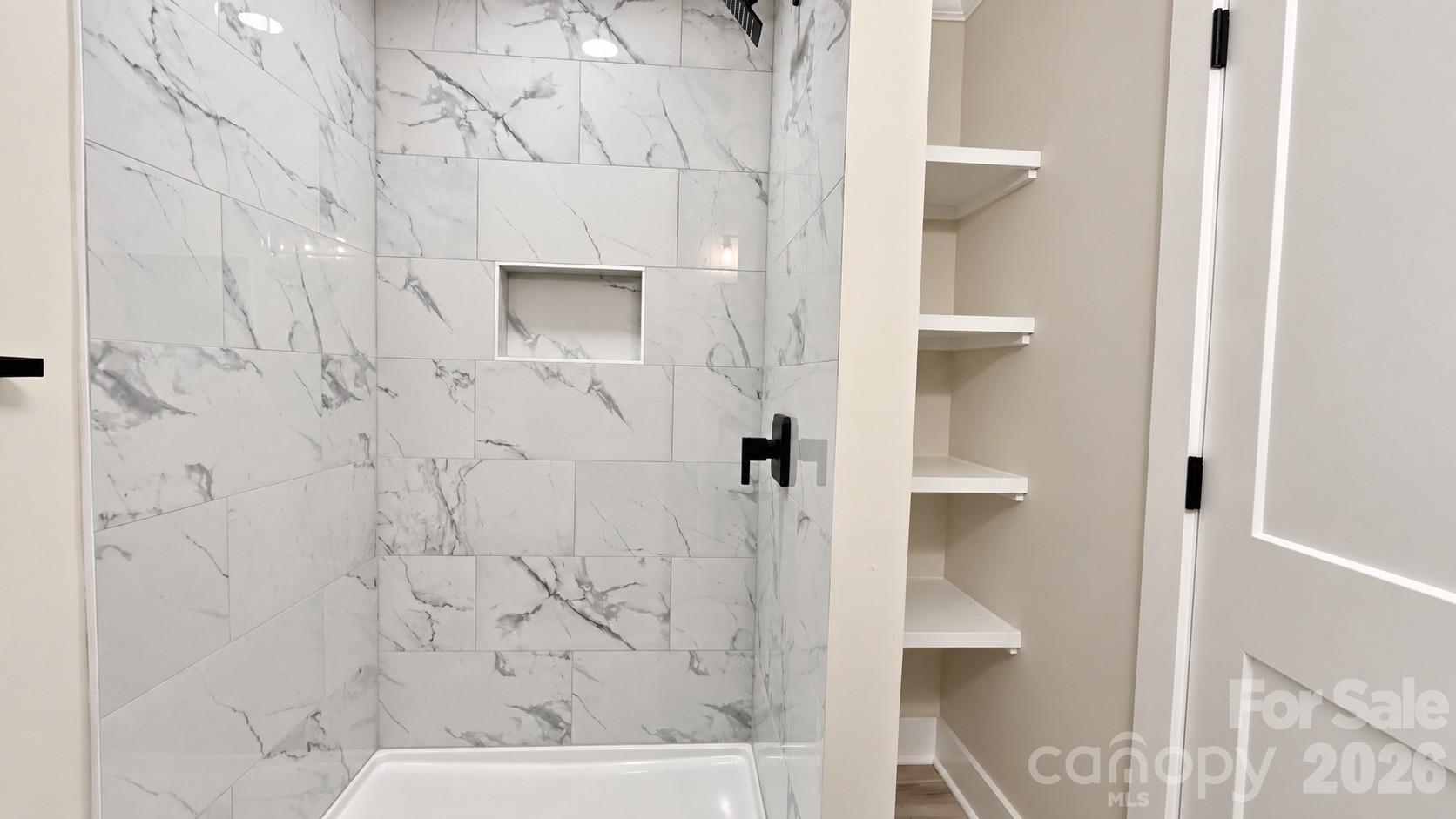 Bathroom with a marble-look tiled shower, recessed niche, black fixtures, and open built-in shelves.