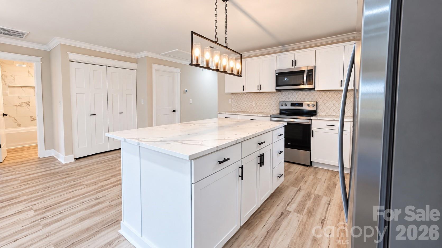 Kitchen with a large white island, stainless steel appliances, patterned tile backsplash, and wood-look floors.