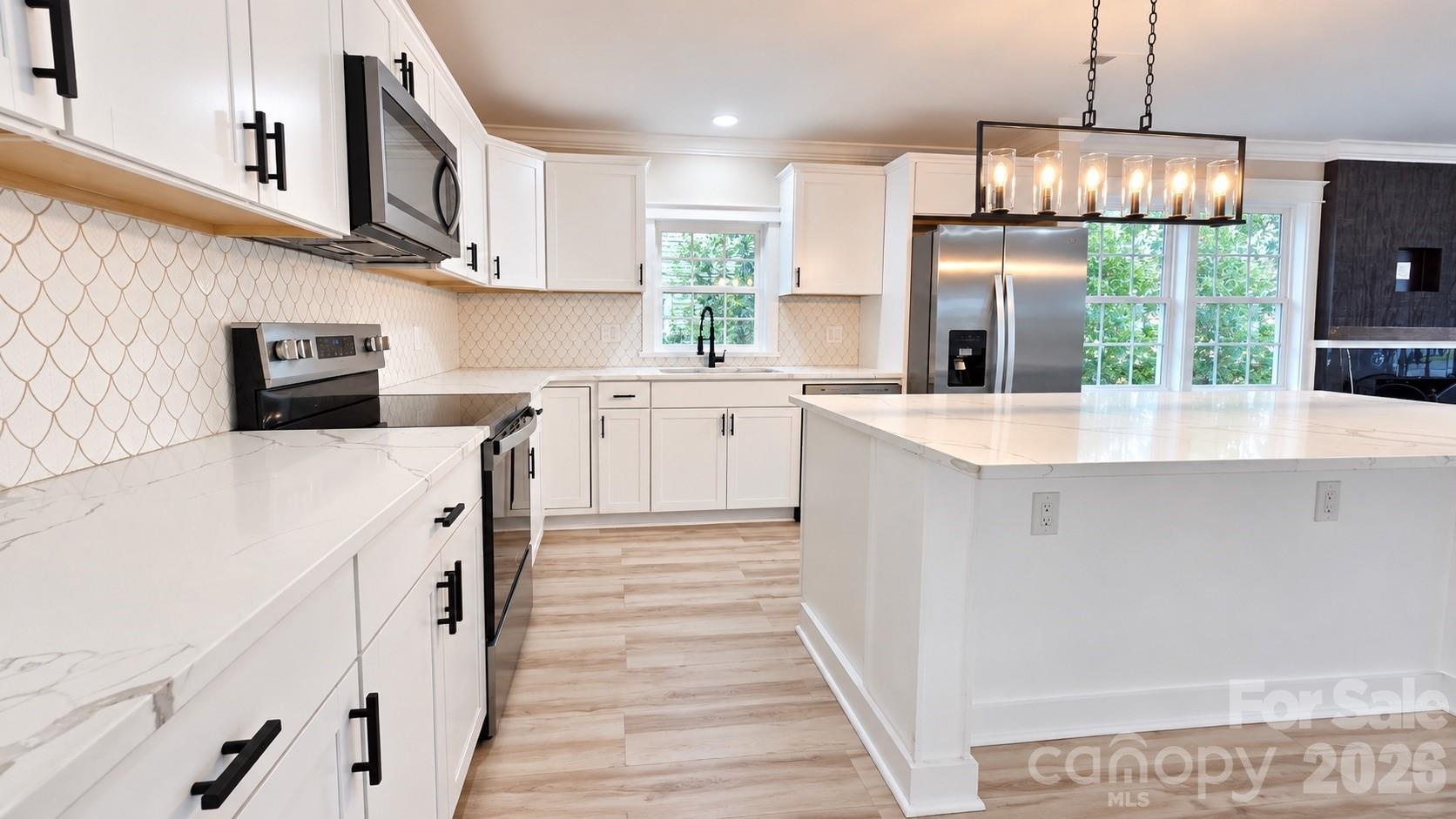 Kitchen with a large white island, marble-look counters, patterned tile backsplash, and stainless steel appliances.