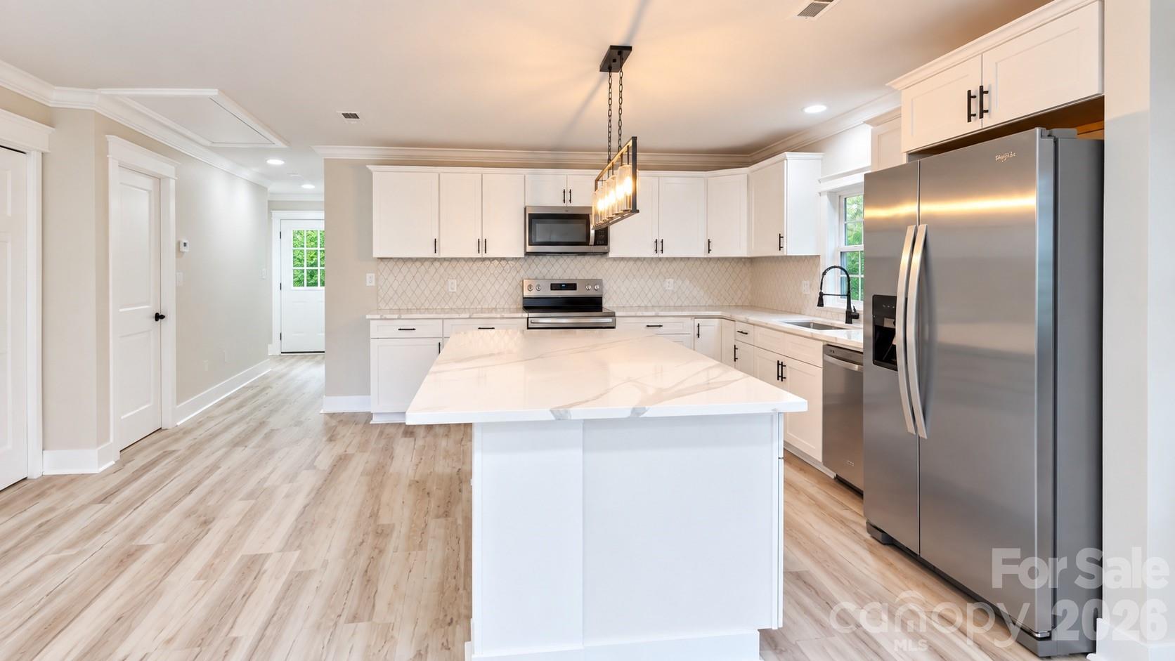 Kitchen with white cabinets, a large island, stainless steel appliances, and light wood-look floors.