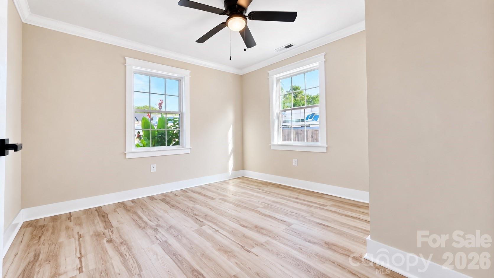 Vacant bedroom with pale wood-look floors, two windows, and a ceiling fan.
