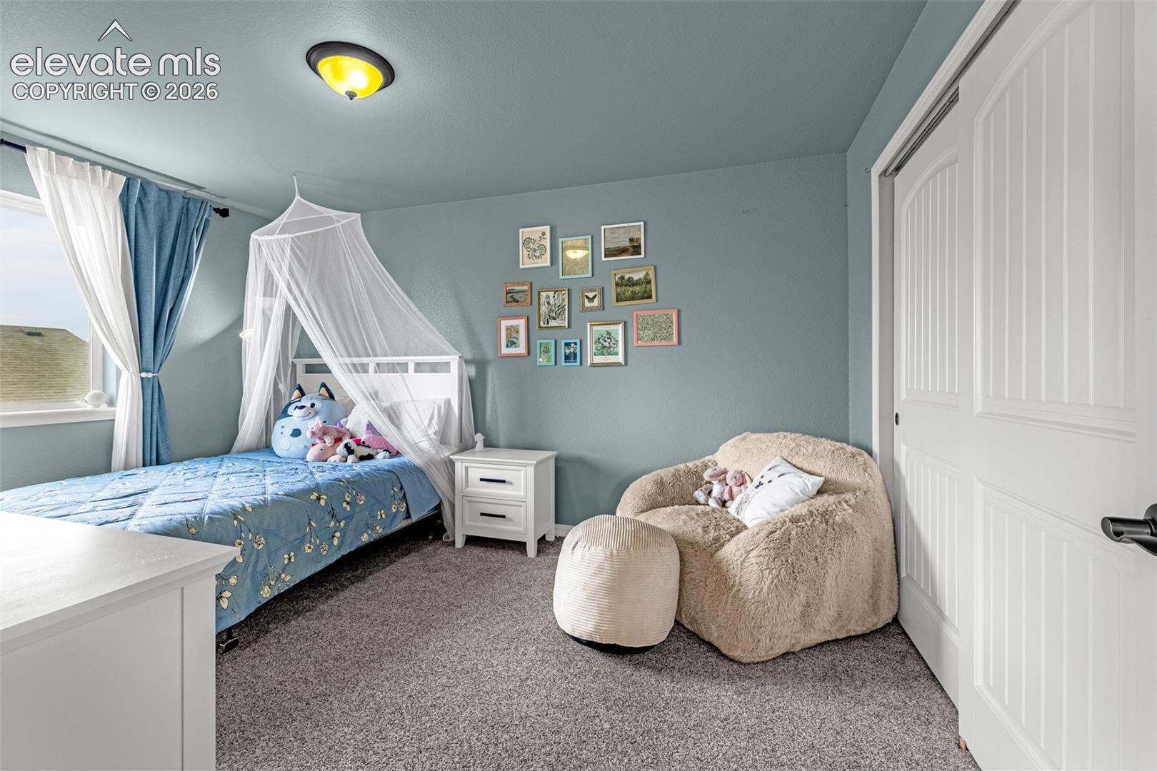 Bedroom with a blue canopy bed, framed wall art, and a plush cream lounge chair.