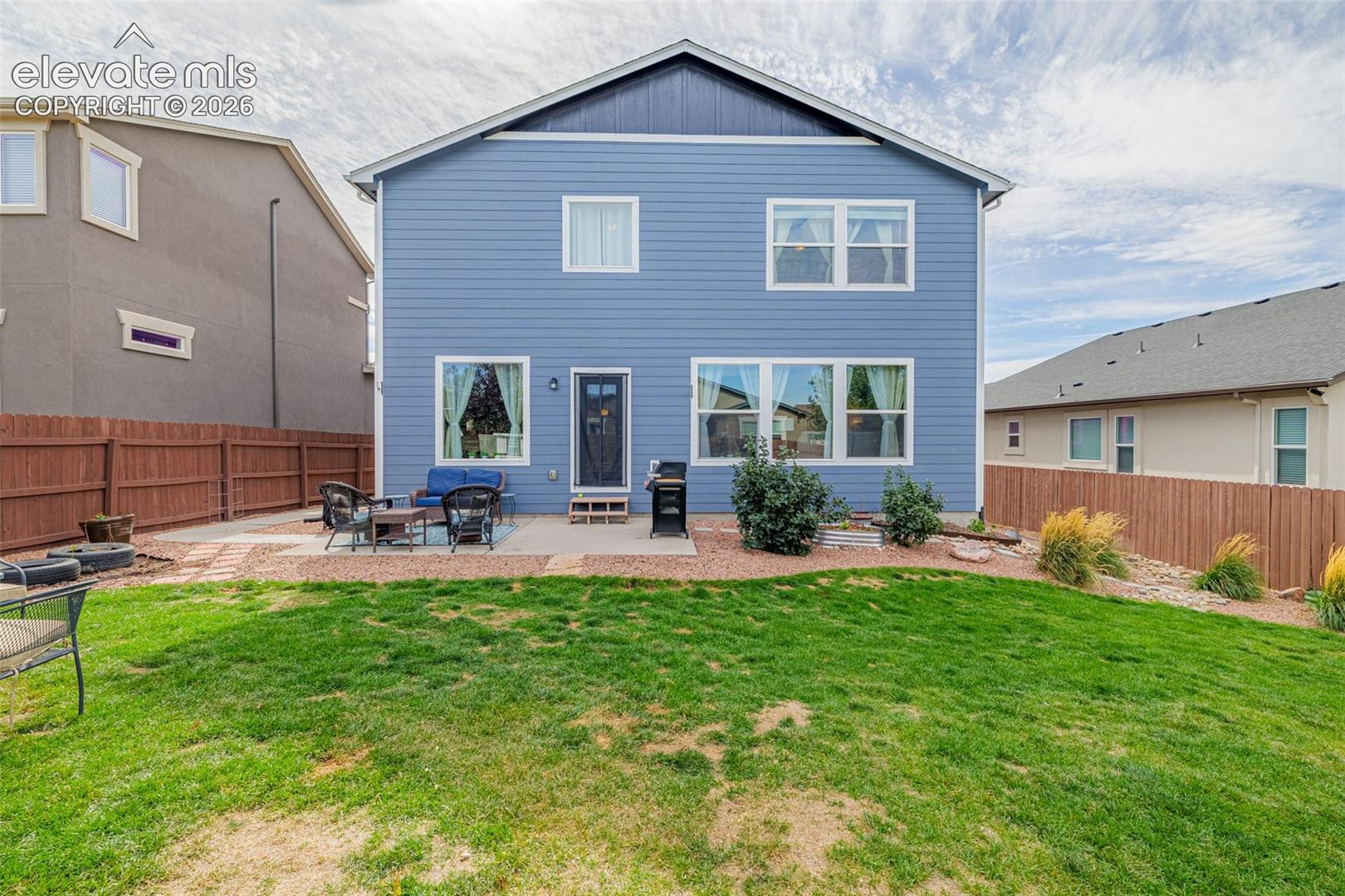 Blue two-story home's rear exterior with a fenced lawn and furnished patio.